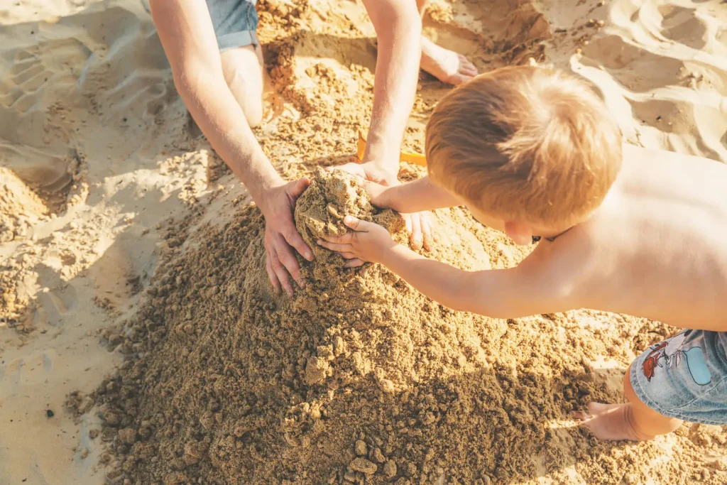 Bambino e adulto giocano con la sabbia in spiaggia.